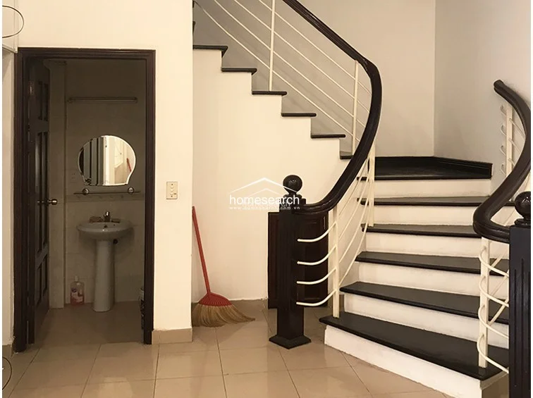 This area showcases a graceful, curved staircase with dark wooden treads and a decorative white railing, serving as a focal point of the home's architecture. Adjacent to the stairs is a compact, functional powder room equipped with a pedestal sink and a wall-mounted mirror, maintaining a clean and well-maintained aesthetic.