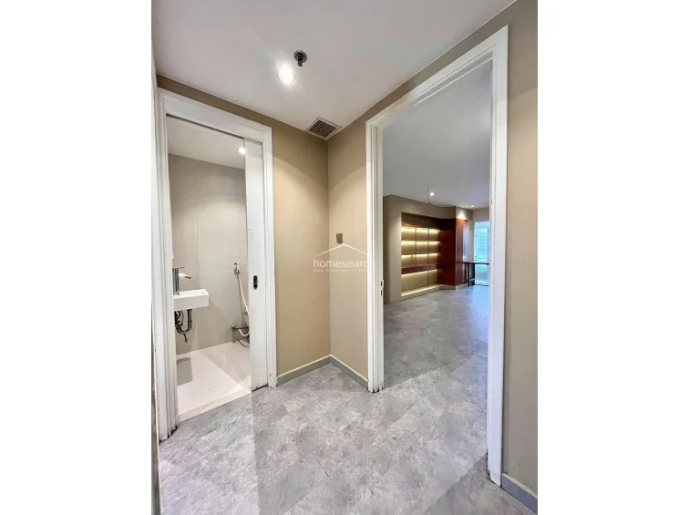 This view shows a hallway leading into a secondary room, with a compact bathroom featuring a wall-mounted sink and tiled surfaces on the left. The interior design is cohesive, utilizing warm beige wall tones and contemporary lighting to create a seamless flow between the functional zones.
