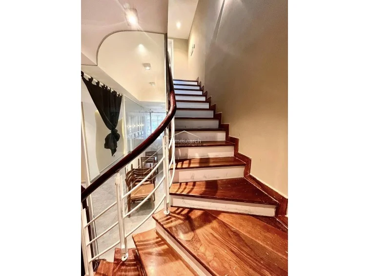 The staircase features elegant dark wood treads and a white curved railing, creating a sophisticated architectural focal point within the property. A large, curved mirror reflects the adjacent room, adding depth and a sense of openness to the circulation area while maintaining a high standard of maintenance.