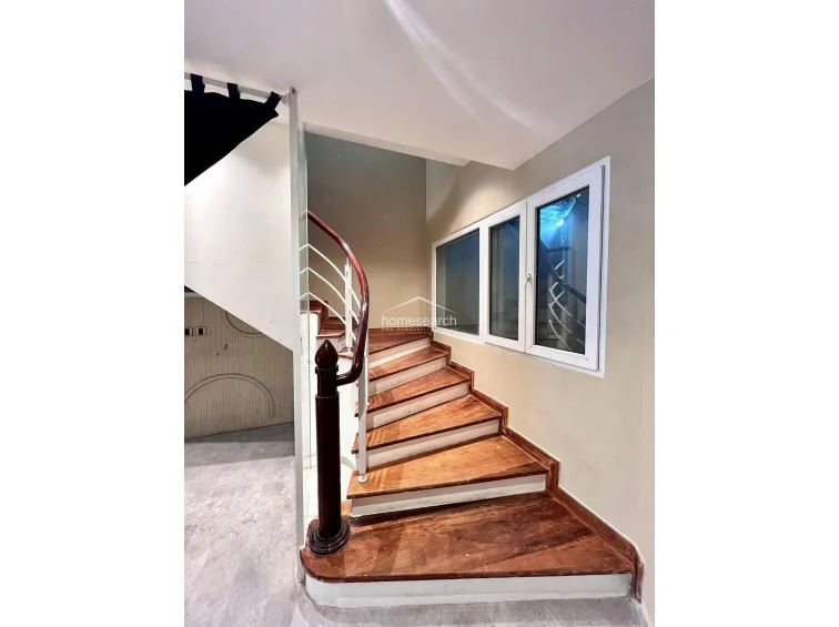 This image displays a staircase featuring warm-toned wooden treads and a classic dark wood handrail, contrasted by a white balustrade. The area is illuminated by natural light entering through a series of white-framed windows, creating an airy transition between levels.