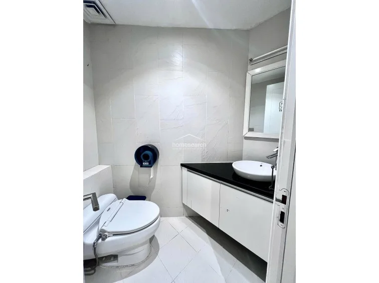 This bathroom features a sleek, modern vanity with a white vessel sink and a contrasting black countertop. The space is well-lit with recessed lighting and includes a wall-mounted mirror, white tiled walls, and a clean, efficient layout.