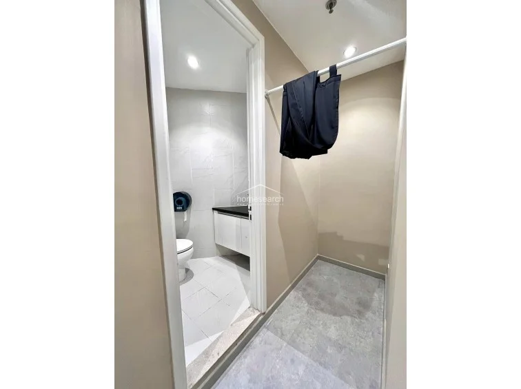 This view shows a small dressing area or walk-in closet space adjacent to the bathroom, featuring a simple garment rail for storage. The neutral color palette and recessed ceiling lighting provide a functional and uncluttered transition zone.