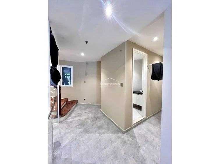 This hallway area connects the staircase to a private bathroom and a small dressing or storage nook. The space features neutral beige walls and modern grey tiled flooring, maintaining a clean and minimalist aesthetic throughout the transition.