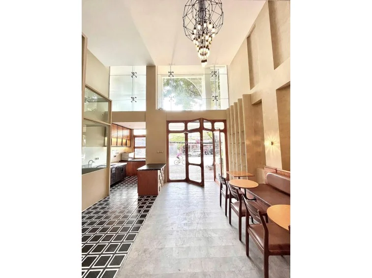 This perspective highlights the impressive double-height ceilings and a dramatic, modern geometric chandelier that serves as a focal point. The space transitions from a light-toned stone floor in the dining area to a striking black-and-white geometric tiled floor in the kitchen zone, creating a clear visual separation between service and seating.