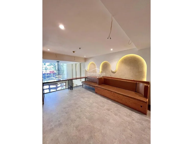 This perspective highlights the flow of the room, showcasing the long built-in wooden seating area that leads toward a large window overlooking the exterior greenery. The space is bright and airy, utilizing a warm color palette for the furniture that contrasts nicely with the cool-toned, durable flooring.