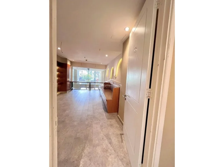 This view from the doorway captures the transition between rooms, emphasizing the clean lines and the cohesive design language of the property. The space is well-maintained and features a neutral, professional atmosphere suitable for a home office or creative studio, with clear sightlines extending to the window at the far end.