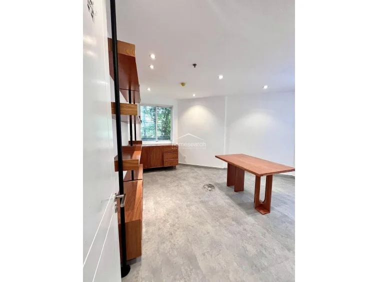 This perspective highlights the open layout of the room, emphasizing the clean lines of the wooden shelving and the spacious feel provided by the white walls. The room maintains a professional, uncluttered atmosphere, with the window offering a view of greenery outside, enhancing the connection to the outdoors.