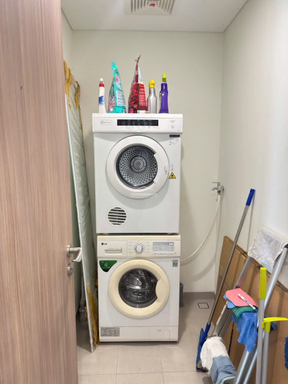 This compact laundry area features a stacked Electrolux dryer and LG washing machine, maximizing vertical space efficiently. The room is finished with neutral-toned walls and tile flooring, providing a clean, utilitarian environment for household chores.