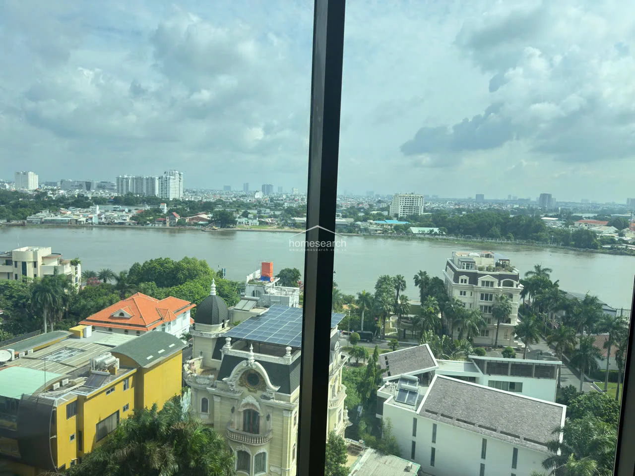 This close-up view captures the impressive, high-elevation perspective of the riverfront area, including neighboring villas and lush greenery. The large, clear glass panes provide excellent natural light and an immersive connection to the surrounding urban landscape.