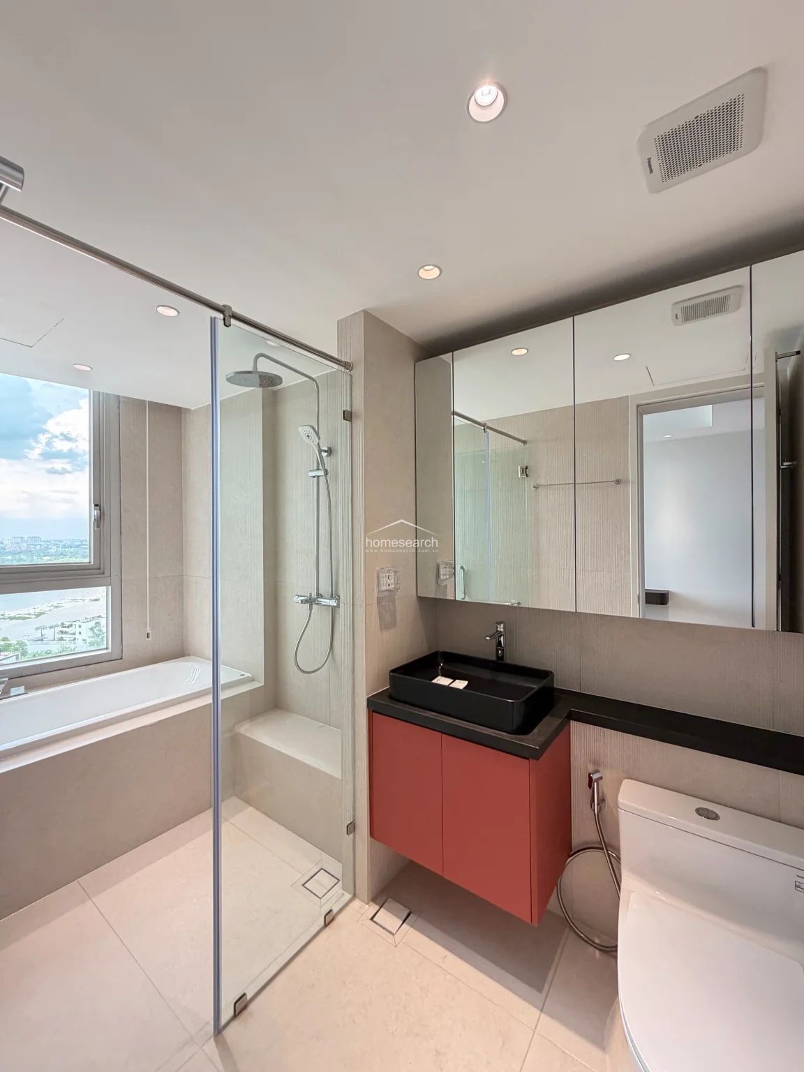 This contemporary bathroom features a luxurious wet-room layout with a glass-enclosed shower and a separate soaking tub positioned by a large window. The space is equipped with a modern black vessel sink, a vibrant red vanity cabinet, and mirrored medicine cabinets, all set against neutral, high-quality wall and floor tiles.