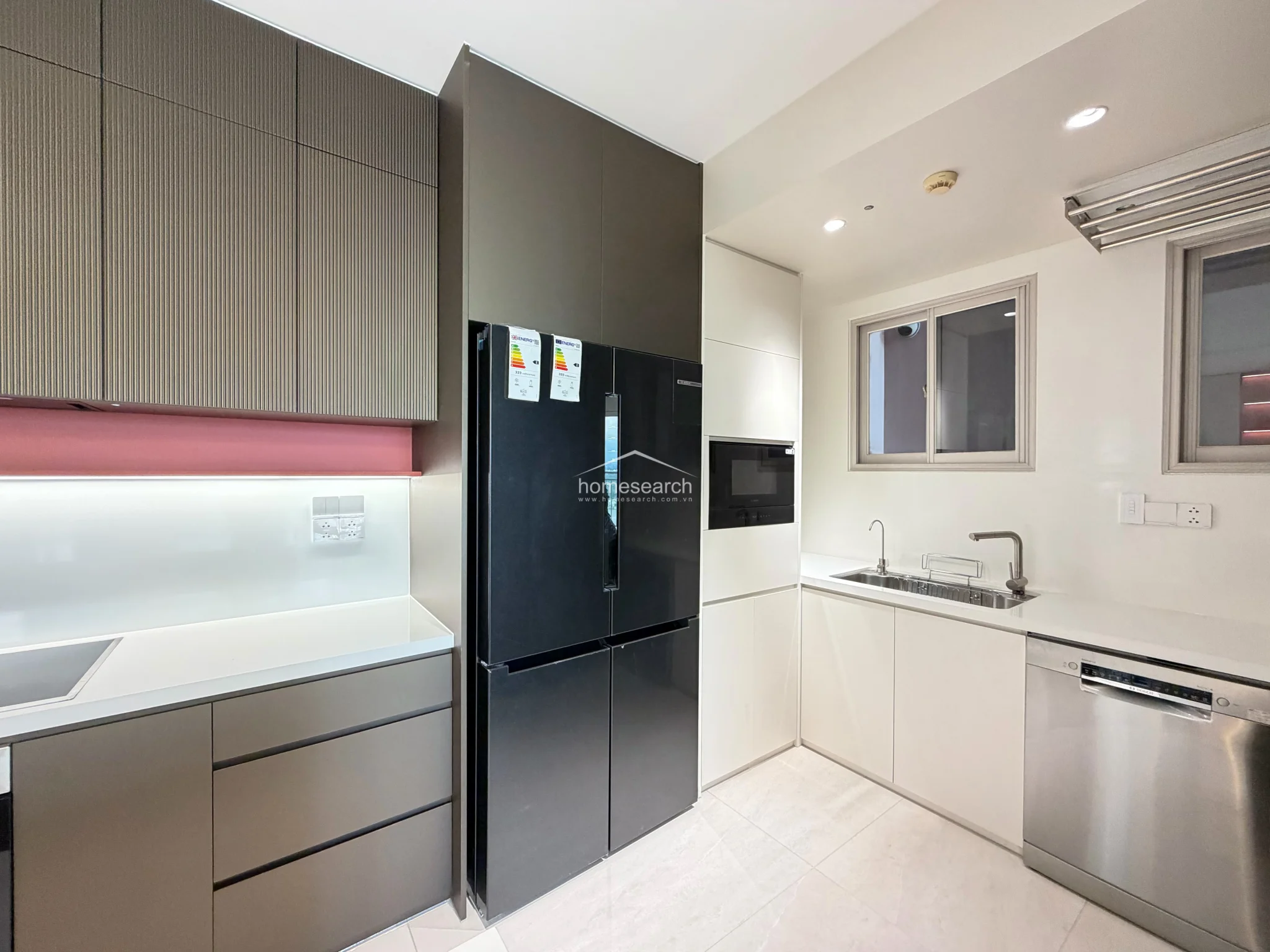 This close-up of the kitchen highlights a contemporary design with a unique pink accent shelf and integrated under-cabinet lighting. The area is highly functional, featuring a stainless steel dishwasher, a modern sink, and a built-in microwave, all maintained in excellent, pristine condition.
