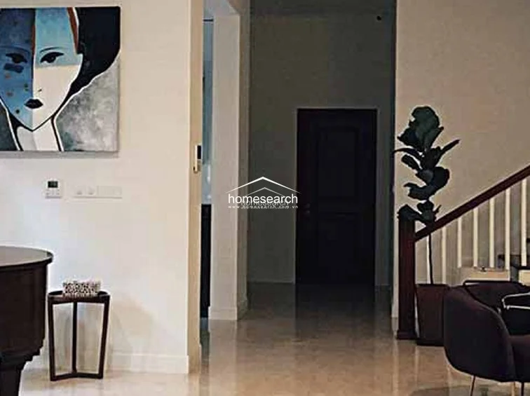 This entryway features polished light-colored tile flooring and a neutral color palette that creates a clean, sophisticated atmosphere. The space includes a grand piano in the foreground and a dark wooden staircase with white balusters, leading into a transition area that connects to other parts of the home.