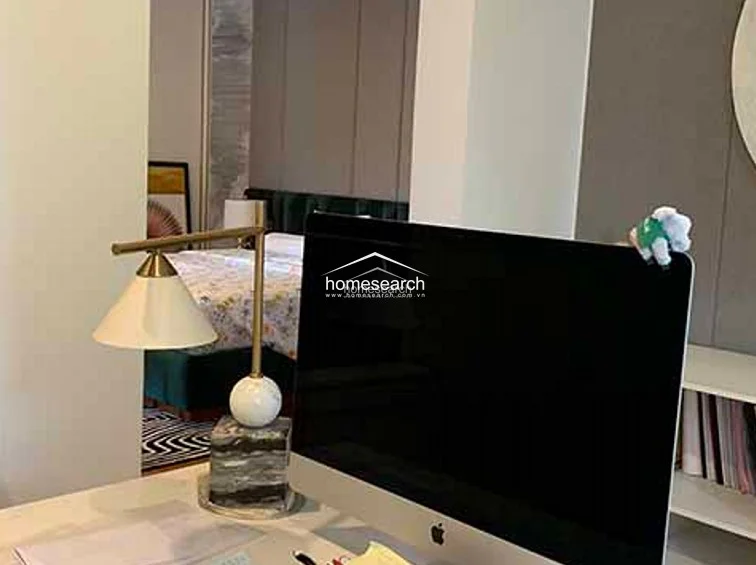 This home office or study area is equipped with a modern Apple desktop computer and a stylish, high-end table lamp featuring a marble base. The room includes neutral-toned wall paneling and built-in shelving, creating a sophisticated and organized workspace.