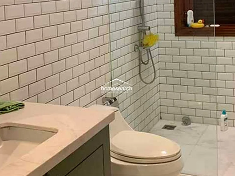 This bathroom features a clean, contemporary aesthetic with white subway-tiled walls and a glass-enclosed shower area. The space is equipped with a modern toilet and a vanity, maintaining a bright and functional atmosphere with a small window for ventilation.