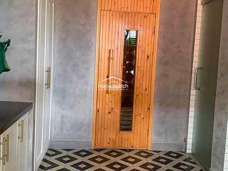 This utility or wellness room features a unique sauna with a vertical wooden door and a geometric patterned tile floor. The walls are finished in a textured grey plaster, providing a contemporary contrast to the warm wood tones and integrated storage cabinetry.