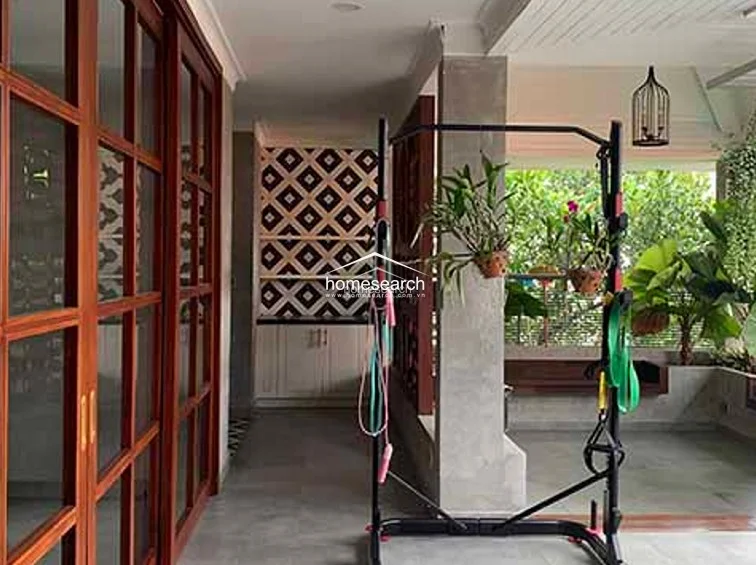 This image captures a semi-outdoor terrace or gym area featuring a concrete-style pillar, a pull-up station, and lush hanging greenery. The space is accented by a decorative geometric-patterned wall and built-in cabinetry, offering a unique blend of fitness utility and tranquil garden aesthetics.