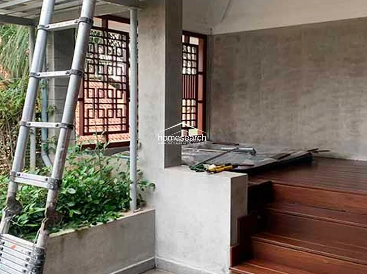 This outdoor terrace features a raw, industrial aesthetic with exposed concrete walls and a wooden stepped platform. The space is accented by decorative wooden lattice screens and a built-in planter box, currently undergoing maintenance with a ladder present.