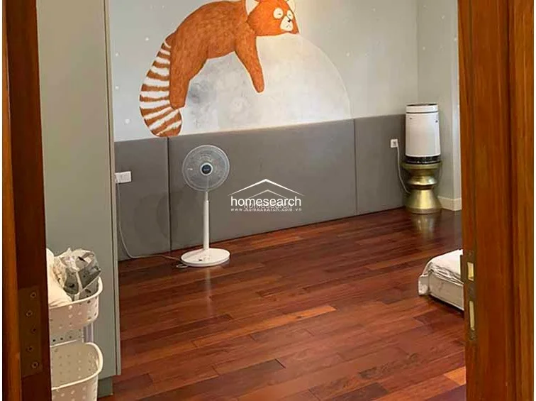 This children's bedroom is characterized by a whimsical, hand-painted mural featuring a red panda and starry night theme. The room includes dark wood flooring, a grey upholstered headboard wall, and a portable air purifier, presenting a well-maintained and playful environment.
