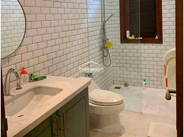 This modern bathroom features a clean, minimalist aesthetic with classic white subway tiles on the walls and light-toned flooring. It includes a sleek vanity with a marble countertop, a circular wall mirror, and a glass-enclosed shower area that maintains an open and airy feel.