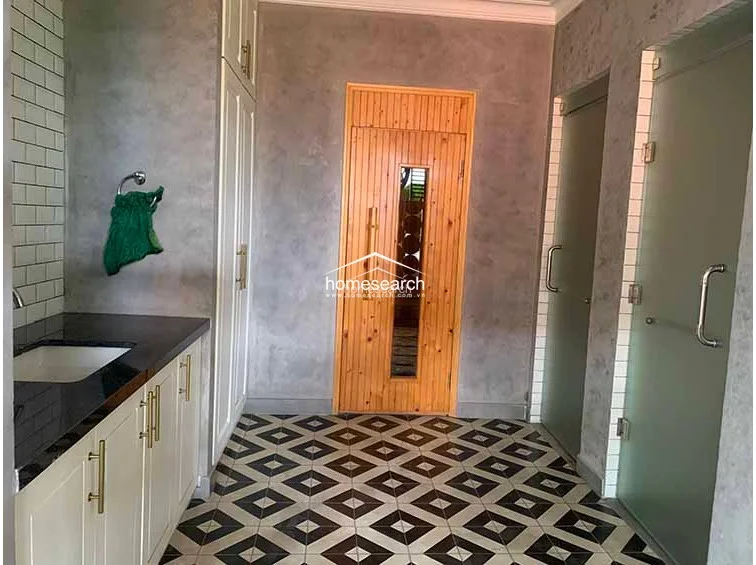 This functional utility or spa-adjacent space features striking geometric patterned floor tiles and textured gray walls that provide a contemporary industrial look. It is equipped with custom white cabinetry for storage, a sleek vanity with a black countertop, and a wooden door leading to an additional room, showcasing excellent organization and modern finishes.
