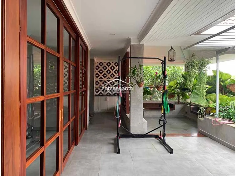 This semi-outdoor terrace area functions as a private fitness space, featuring large wooden-framed glass sliding doors that connect to the interior. The space is finished with neutral grey floor tiles and includes a built-in storage cabinet with a decorative geometric pattern, contributing to a well-maintained, contemporary aesthetic.