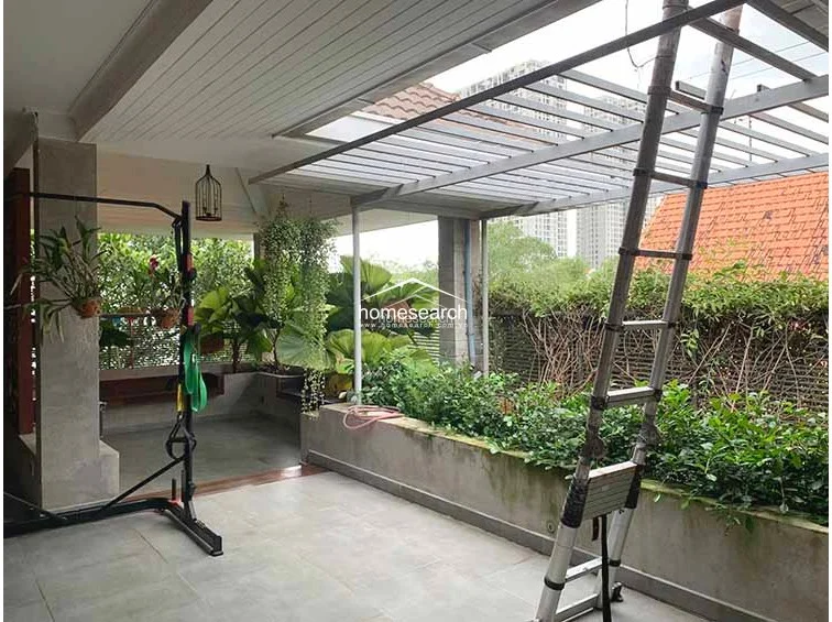 This view highlights the terrace's transition into a lush garden area, framed by a modern metal pergola structure that provides partial shade. The area is bordered by concrete planter boxes filled with greenery, offering a serene, private outdoor retreat with a well-kept, architectural feel.