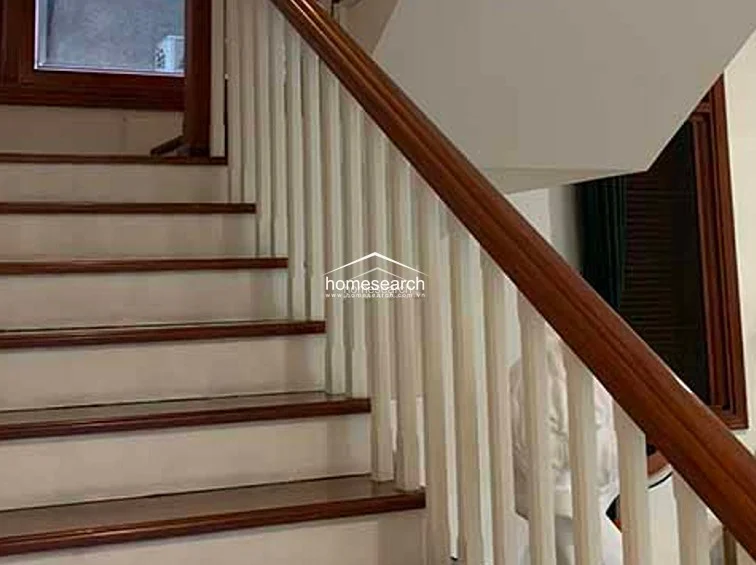 This staircase showcases a classic design with polished wooden treads and crisp white risers, complemented by a sturdy wooden handrail and white balusters. The architectural flow connects the levels seamlessly, while the adjacent large window allows natural light to filter into the stairwell, highlighting the well-maintained condition of the woodwork.