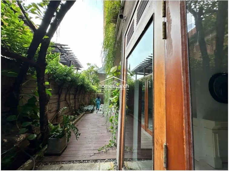 This outdoor side walkway features a rich wooden deck bordered by a tall wall covered in lush climbing vines and greenery. The space offers a serene, private transition area that connects to the interior via large glass doors, enhancing the home's indoor-outdoor flow.