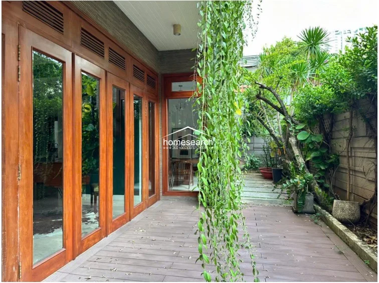 This outdoor terrace is framed by expansive wooden-framed glass doors that provide a seamless transition to the interior living spaces. The area features durable decking and lush vertical greenery, offering a private, tranquil garden view.