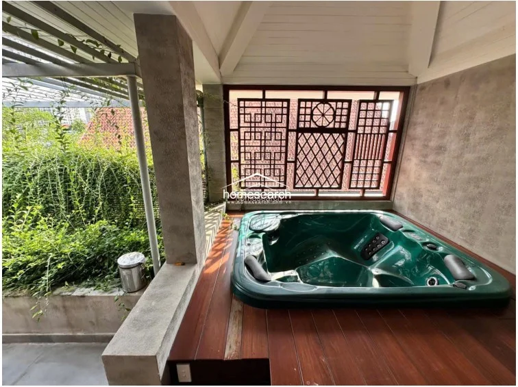 This private spa area is designed for relaxation, featuring a built-in jacuzzi set against a decorative wooden lattice screen. The space is surrounded by natural greenery and concrete architectural elements, emphasizing a high-end, resort-style maintenance level.