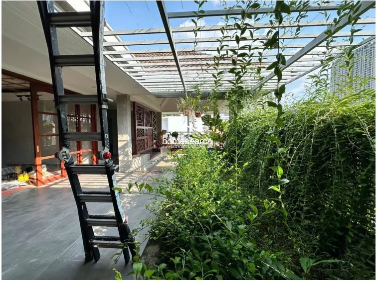 This view highlights the transition between the interior living space and the outdoor terrace, sheltered by an open metal pergola structure. The area is defined by a lush, vertical garden wall and large-format floor tiles, suggesting a modern, nature-integrated design.