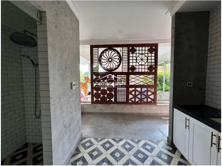 This unique space features a striking blend of industrial and decorative elements, including a walk-in shower with white subway tiles and a decorative wooden lattice screen that overlooks the outdoors. The flooring transitions from a bold geometric patterned tile to a neutral stone, creating a distinct separation between the wet area and the open-air terrace.