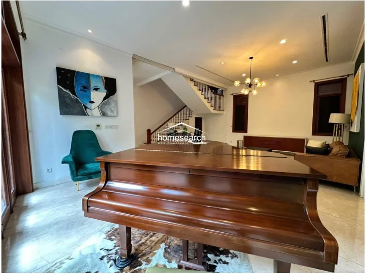 This expansive living area is anchored by a grand wooden piano and features elegant marble flooring throughout. The space is illuminated by a striking modern chandelier and flows openly toward a staircase, showcasing a high-end, well-maintained interior design.