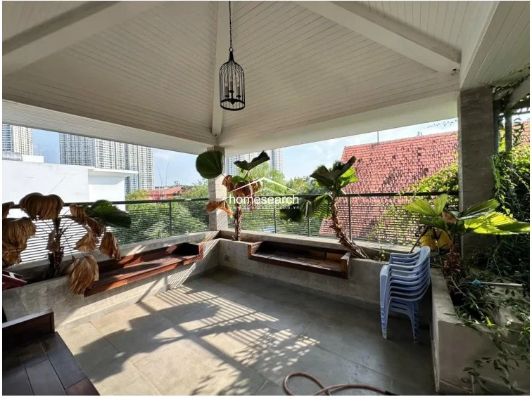 This spacious covered balcony features a high, vaulted ceiling with white wood paneling and a decorative pendant light. The space is finished with concrete flooring and built-in wooden bench seating, offering a scenic view of the surrounding neighborhood and high-rise buildings.