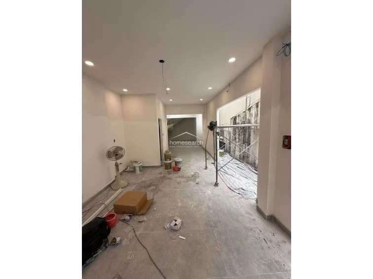 This interior space appears to be an open-plan living or commercial area featuring a neutral white color scheme and recessed ceiling lighting. The room flows into a deeper section of the house, with a large side opening that currently exposes the structure to an adjacent light well or exterior wall.
