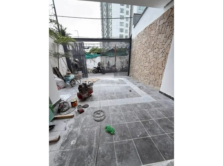 This ground-floor outdoor area serves as a driveway or courtyard, finished with large-format grey stone tiles and a decorative natural stone accent wall on the right. The space is currently being used as a staging area for construction, indicating that the property is in the final stages of completion.
