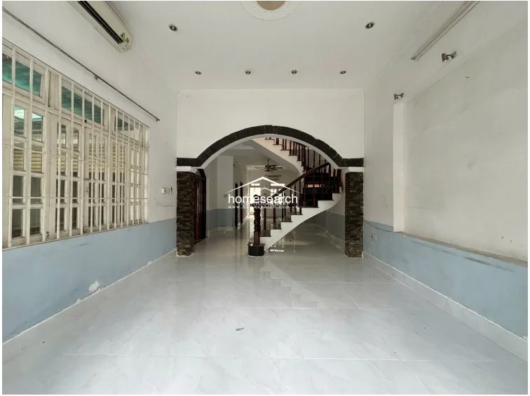 The main living area features an open-concept layout defined by a striking arched entryway that leads to a wooden staircase. The space is finished with light-colored tile flooring, pale blue lower wall accents, and recessed ceiling lighting, with an AC unit already installed for climate control.