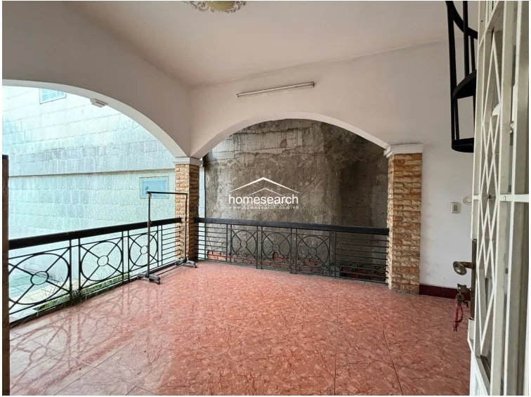 This expansive outdoor terrace features a covered area with elegant architectural arches and stone-accented pillars. The space is finished with reddish-brown tile flooring and a black metal safety railing, offering a versatile area for outdoor living or laundry drying.