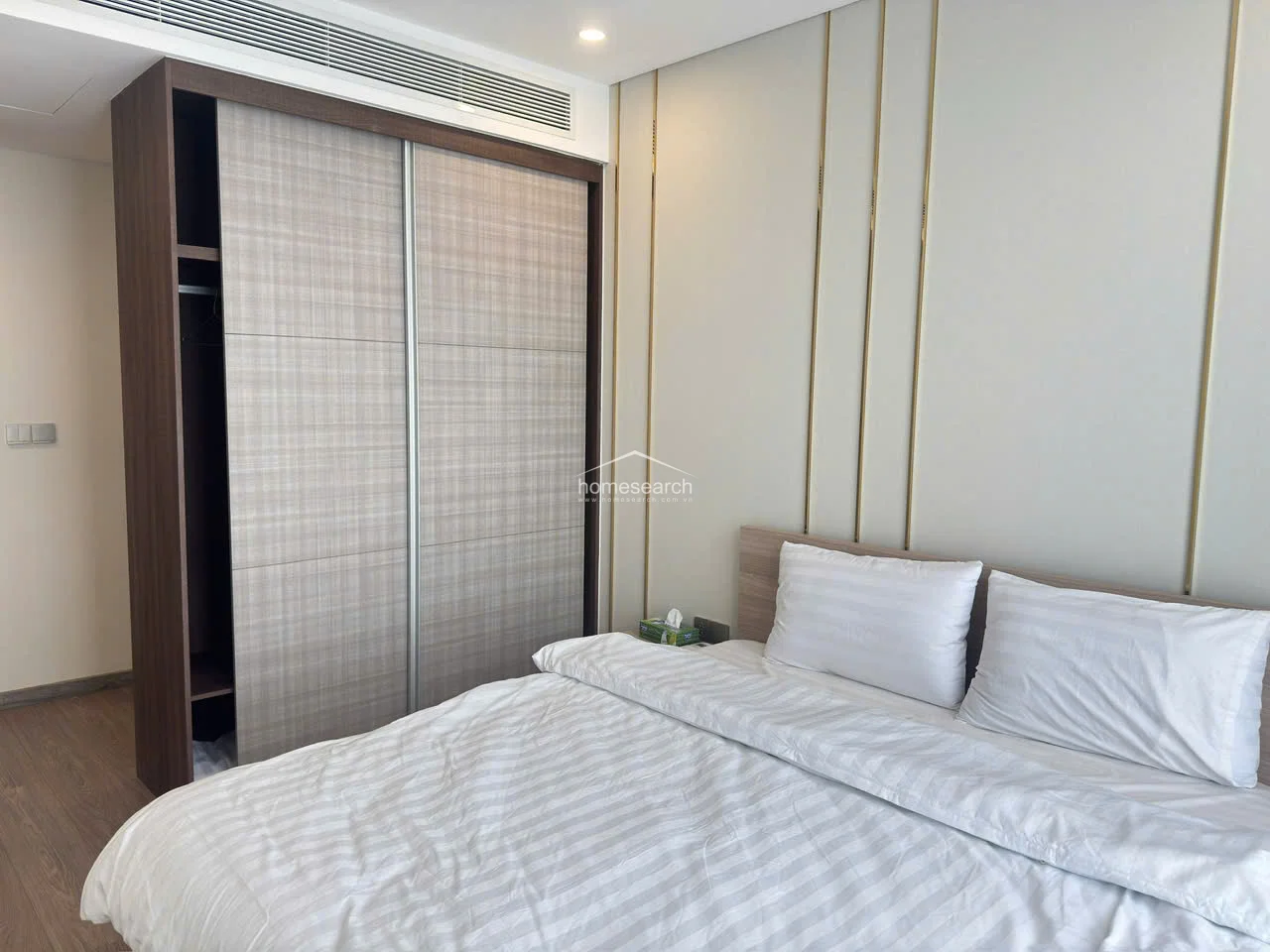 This shot showcases the cohesive design of the bedroom, highlighting the seamless integration of the wardrobe and the bed area. The room maintains a high level of maintenance, with clean lines and a consistent warm-toned color scheme that promotes a relaxing environment.