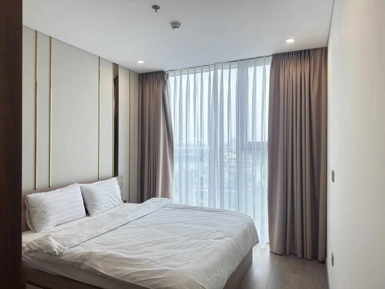 This perspective emphasizes the bedroom's bright and airy atmosphere, provided by the expansive window that allows for significant natural light. The neutral color palette and high-quality finishes, including the recessed ceiling lighting, reflect a well-maintained and contemporary living space.