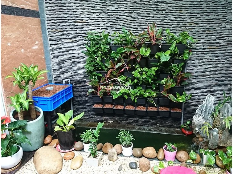 This outdoor space features a vertical garden wall mounted on textured stone, creating a serene and natural focal point. A small water feature and a collection of potted plants add to the tranquil environment, which is finished with a gravel floor. This area is well-maintained and serves as a decorative, peaceful retreat within the property.