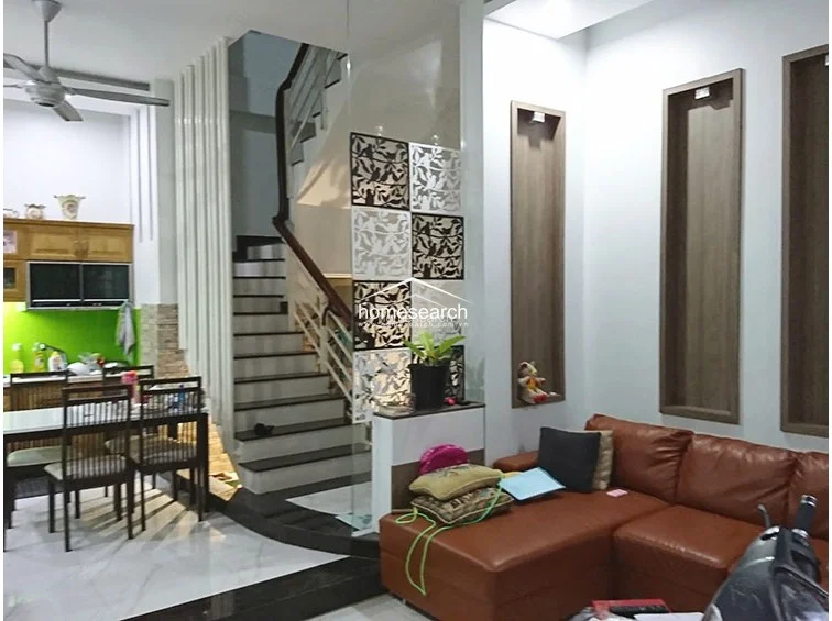 The living room is anchored by a large, brown L-shaped leather sofa and features unique architectural wall niches for display. A decorative laser-cut screen separates the seating area from the staircase, while the space flows directly into the adjacent kitchen and dining zone.