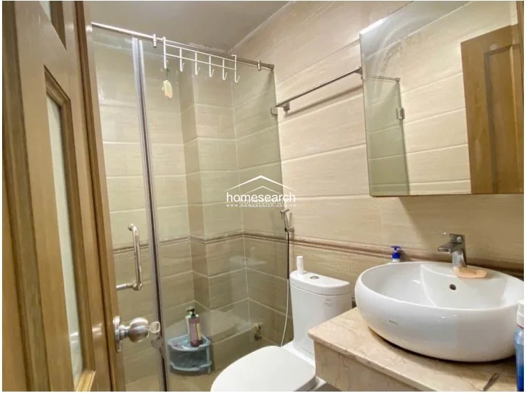 The bathroom is finished with neutral-toned wall tiles and features a modern glass-enclosed shower stall for efficient space usage. It includes a vessel sink set on a stone vanity top and a large wall mirror, reflecting a clean and functional design in good condition.