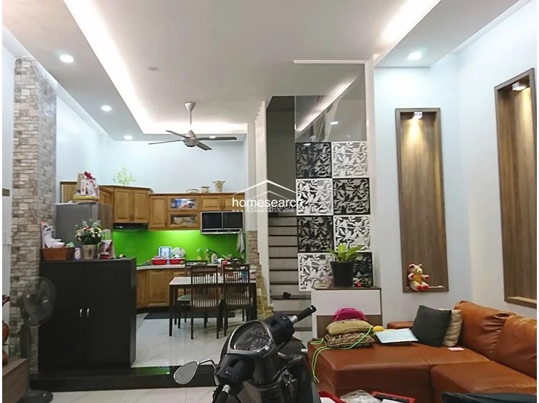 This open-concept living and dining area showcases a contemporary design with a brown leather sofa and decorative wall niches. The space is divided by a stylish, patterned room divider that separates the living room from the staircase and kitchen area. The neutral color palette and recessed lighting create a cohesive and inviting atmosphere.