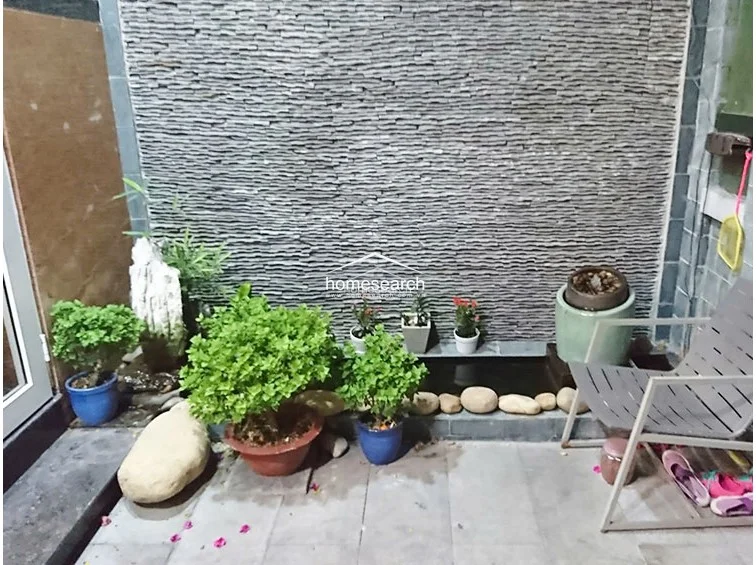 This tranquil outdoor terrace features a textured stone feature wall and a small water feature, creating a serene garden-like atmosphere. The area is paved with neutral tiles and includes potted greenery, offering a private, well-maintained space for relaxation.