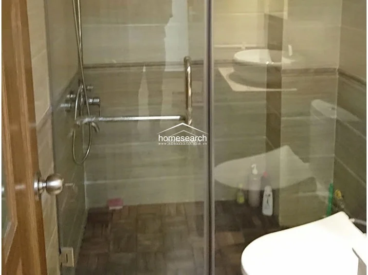 This bathroom is designed with a contemporary walk-in shower enclosure featuring a glass door and modern chrome fixtures. The space is finished with warm-toned wall tiles and a dark, textured floor, maintaining a clean and functional condition.