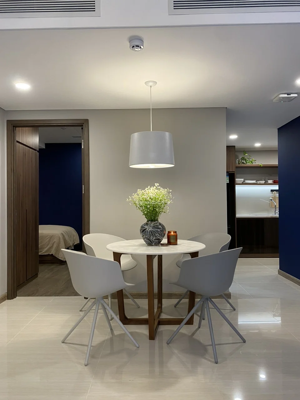 This view highlights the functional layout of the dining area, which is positioned adjacent to a sleek kitchen featuring dark wood cabinetry and integrated appliances. The space is well-maintained and minimalist, utilizing recessed ceiling lighting and a contemporary pendant lamp to define the dining zone.