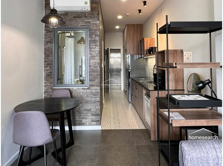 This studio apartment features an efficient, open-concept layout that flows from the entryway kitchen into a combined living and sleeping area. The space is well-maintained with a modern industrial aesthetic, highlighted by a brick accent wall, matte black fixtures, and large-format dark floor tiles.