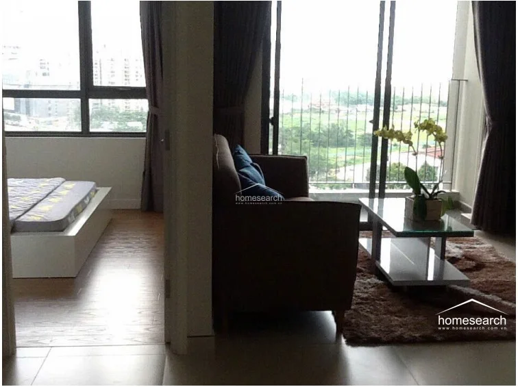 This living space is connected to the bedroom, creating a cohesive flow between the sleeping and lounging areas. The room features a comfortable sofa, a glass-topped coffee table, and a decorative orchid, all framed by large windows that offer expansive outdoor views and plenty of natural light.