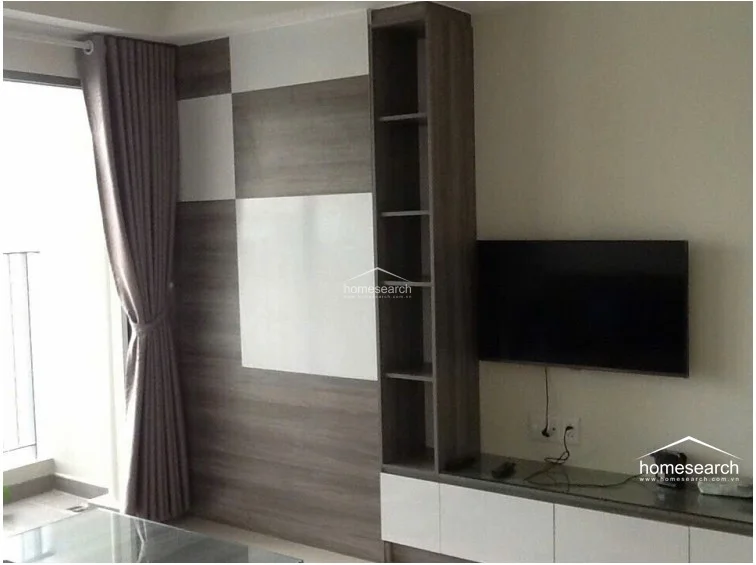 This living space is characterized by a modern, custom-built media wall featuring a combination of wood-grain and white panels with integrated vertical shelving. A flat-screen TV is wall-mounted above a sleek, low-profile storage console, creating a clean and organized entertainment area adjacent to a balcony.